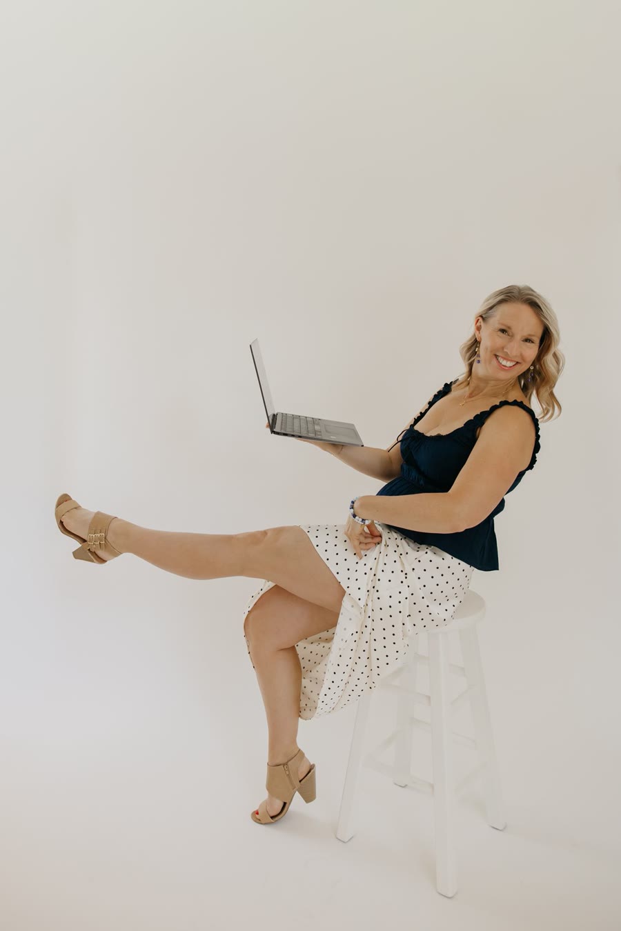Kristen laughing and kicking up a leg while holding her laptop