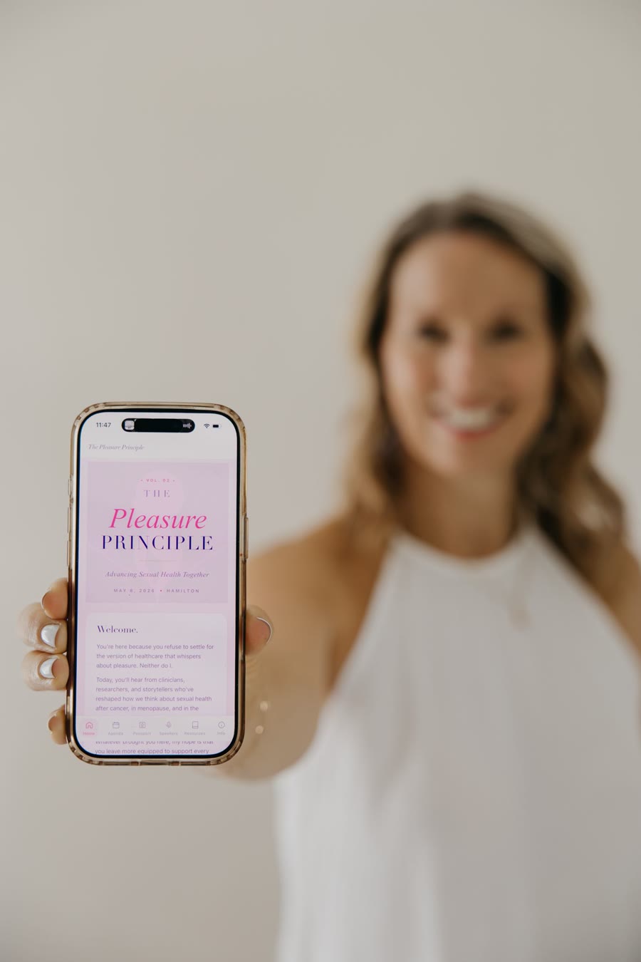 Kristen holding up her phone showing the Pleasure Principle conference app she built